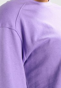 Felpa di cotone lilla con scollo a giro, maniche lunghe a raglan e una texture morbida con dettagli di cucitura sottili.