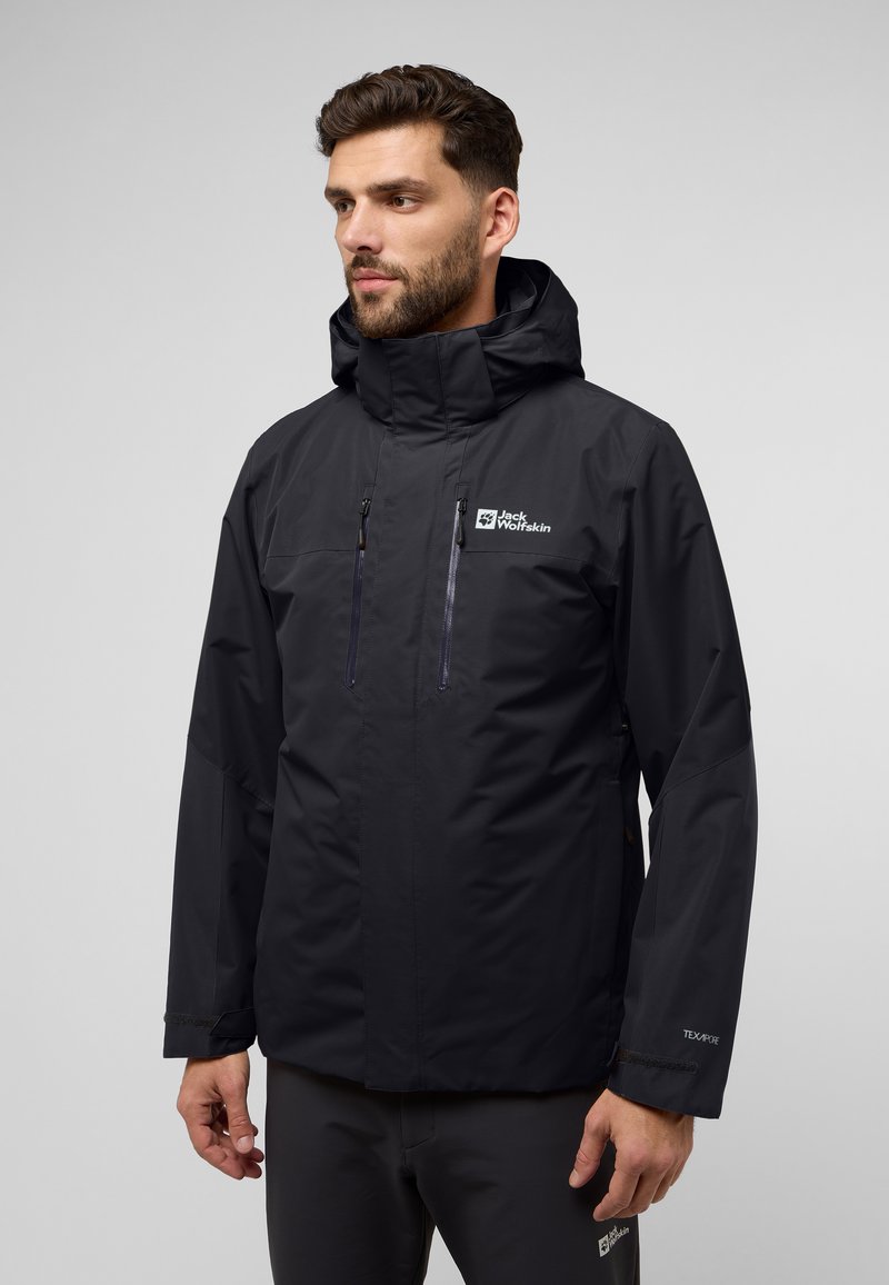 Veste noire imperméable avec un col haut, deux poches zippées sur la poitrine et des poignets ajustables. Présente le logo Jack Wolfskin sur la poitrine.
