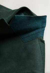 Donkergroene jas met een gestructureerde ontwerp, voorzien van een textuur vilt kraag en gladde stof, met zichtbare stiksels en een schuin gesneden snit.