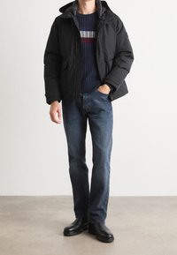 Mustanvärinen toppatakki hupulla, päällä tummansininen, vaakaraitakuvioitu ribbineule. Asuun kuuluu siniset farkut ja mustat saappaat.