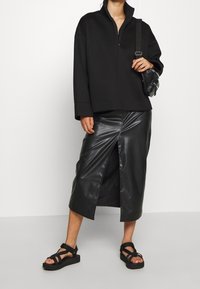 Černý pulovr se zipem a volným střihem; v kombinaci s černou koženou midi sukni s předním rozparkem; černé sandály na tenkých páscích doplňují vzhled.