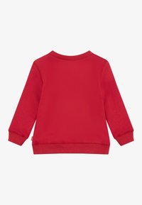 Felpa rossa con maniche lunghe, collo rotondo, polsini e orlo a coste. Tessuto liscio, colore uniforme, senza fantasie o dettagli decorativi.