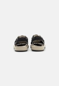 Black sandals with adjustable straps, a cushioned beige sole, and a textured finish. Open back design for easy wear.