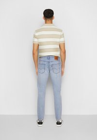 Proužkované béžovo-bílé polo tričko s krátkými rukávy spárované se světle modrými džínami, na kterých je kožená nášivka a zadní kapsy. Černobílé tenisky.