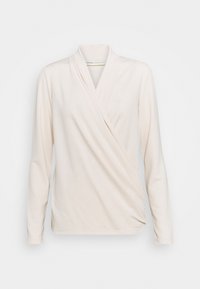 Cremefärgad långärmad omslagblus med V-ringning och draperad sidodetalj, uppvisad mot en neutral vit bakgrund.