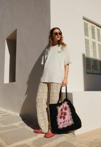 Oversized light gray t-shirt with a colorful graphic, beige patterned crochet pants, and a black tote bag with pink tomato design. Pink slip-on shoes.