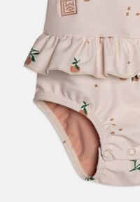 Lys rosa badedrakt med volanger i kanten, med små oransje mønstre og grønne blader. Mykt materiale, trykknapper nederst.