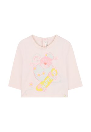 Chemise en coton rose pâle à manches longues présentant un graphique pailleté d'un lapin sur un skateboard avec le texte « HEUREUX » en jaune et des accents floraux.