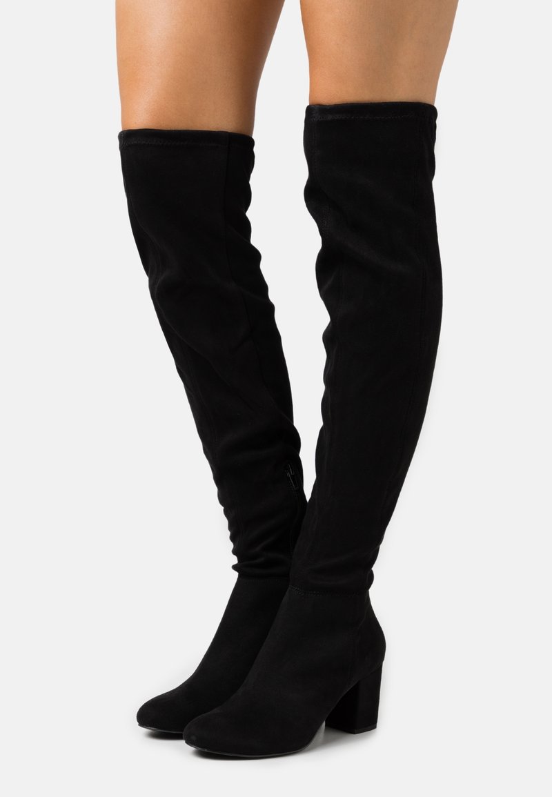 Bottes en suede noir à hauteur de genou avec une texture lisse, un talon carré, un design ajusté et un léger drapé en haut. Détail de fermeture éclair sur le côté.