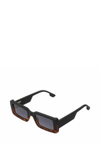 Lunettes de soleil avec une monture carrée présentant un motif noir et écaille de tortue. Verres sombres avec une finition mate sur la monture et des branches élégantes.