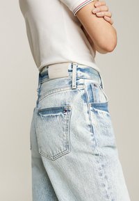 Jeans de denim azul claro de tiro alto con un acabado desgastado, que cuentan con dos bolsillos traseros y una etiqueta texturizada de Tommy Hilfiger en la cinturilla.