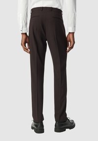 Pantalons marron ajustés avec une finition en tissu lisse, coupe slim, deux poches arrière et passants de ceinture. Associés à des chaussures de ville noires.