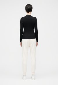 Camisola preta justa de mangas compridas combinada com calças de treino largas de cor creme e ténis brancos, vista de costas contra um fundo simples.