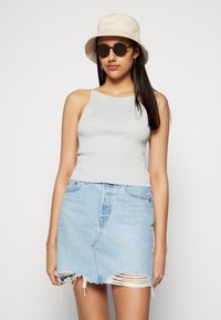 Top de alças riscado em cinza claro combinado com uma saia mini de ganga desfiada em azul claro. A modelo usa um chapéu tipo balde em creme e óculos de sol redondos.