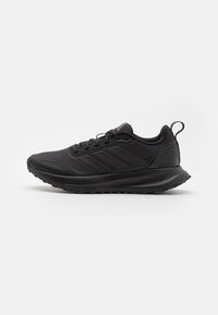 Černá sportovní bota s texturovaným svrškem, gumovou podešví a polstrovaným límcem. Obsahuje tři vyvýšené pruhy a poutko na patě.