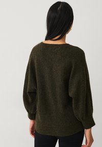 Pull vert surdimensionné avec un col rond, en tissu tricoté texturé et avec des manches bouffantes. Présente un ourlet et des poignets côtelés.