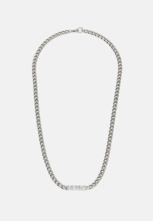 Sølvekæde med "HUGO" navneskilt og rund lås på hvid baggrund.