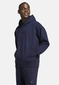 Felpa blu navy realizzata in tessuto morbido, con tasca frontale, polsini a coste e un piccolo logo nero sul petto.