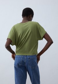 Olive green short-sleeve t-shirt with a relaxed fit, paired with blue denim jeans. Soft fabric with minimal detailing and a loose silhouette.