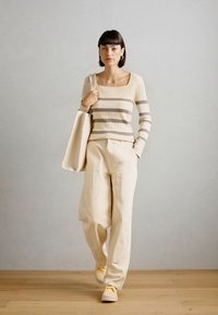 Pulover bej cu dungi taupe orizontale, asociat cu pantaloni largi crem și adidași galbeni, completat de o geantă albă tip tote.