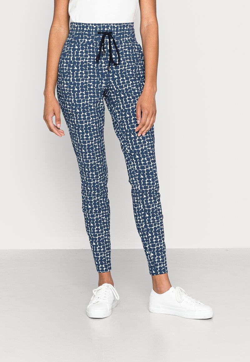 Navy blue patterned leggings with a white abstract design, high waist, drawstring, and a tapered fit. Paired with white sneakers.