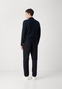 Donkerblauwe trui met een kraag, gecombineerd met donkere broeken en witte sneakers. Het heeft een eenvoudig, slim ontwerp en een soepele textuur.