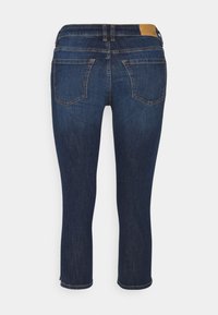 Jeans de mezclilla azul oscuro con pierna recta, que cuentan con dos bolsillos traseros y un parche de cuero marrón en la cinturilla en la parte trasera.