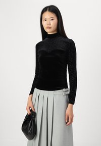 Haut noir à manches longues avec un haut à motif léopard texturé et un corps en velours lisse, associé à une jupe plissée gris clair.