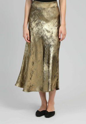 Jupe midi dorée métallisée avec une texture brillante, ourlet évasé et ceinture lisse, accompagnée de ballerines noires.