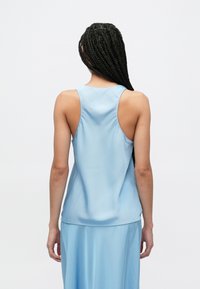 Lyseblå, ermeløs satintopp med rund halsutringning og avslappet passform, med glatt tekstur og minimale sømdetaljer på baksiden.