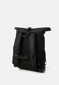 Sac à dos noir à rabat avec des bretelles rembourrées, une boucle au niveau de la poitrine et une poche en mesh sur le côté, montré de dos sur un fond blanc.