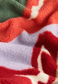 Coperta in pile con un motivo ondulato nei colori: rosso, arancione, verde, lavanda e crema; aspetto texturizzato, morbido e accogliente.