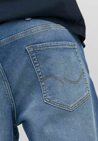 Vaqueros de mezclilla azul claro con una textura desgastada, que presentan un solo bolsillo trasero con un detalle de costura curva en color tostado.