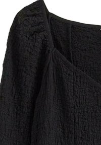 Svart texturerad topp med skrynklig tyg. Har en vid halsringning och intrikata detaljer längs sömmarna. Variabla ytmönster är synliga.