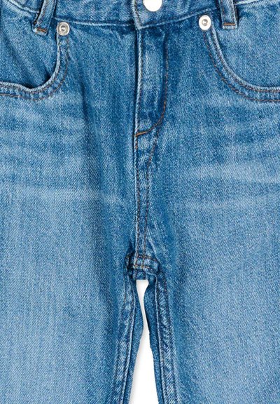 Vue de face d'un jean en denim bleu montrant le bouton, la fermeture éclair et les poches avec des surpiqûres visibles et des rivets métalliques.