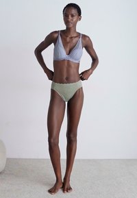 Ανοιχτό μπλε σουτιέν με υφή και ρυθμιζόμενες τιράντες, σε συνδυασμό με πράσινα μπικίνι με σχέδιο. Το μοντέλο στέκεται σε ουδέτερο φόντο.