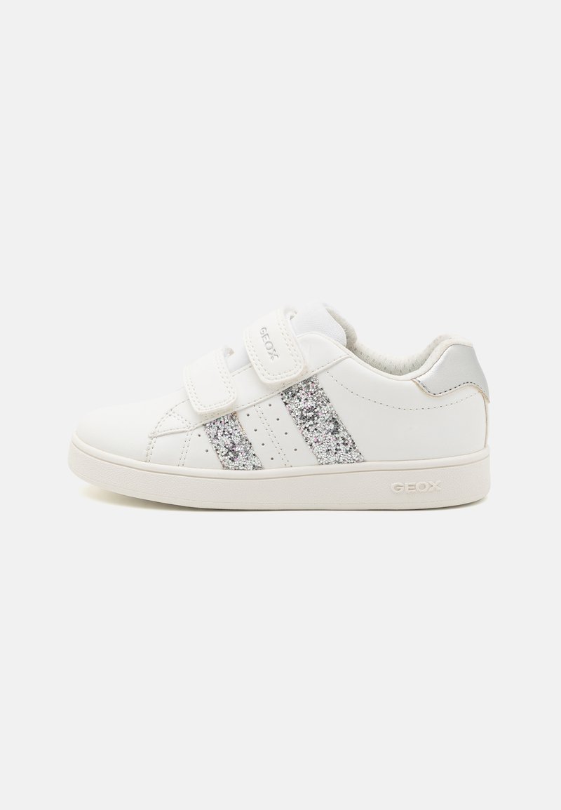 Baskets blanches avec des bandes Velcro, accents gris métalliques et rayures scintillantes sur les côtés. Matière en cuir lisse ; semelle en caoutchouc.
