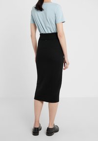 Jupe noire en tricot avec une taille côtelée, assortie à un haut à manches courtes bleu clair. La jupe est ajustée et arrive au genou.