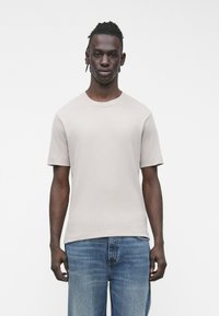 Tricou cu mânecă scurtă, culoare bej deschis, cu o textură striată și gât rotund, asortat cu blugi din denim albastru mediu. Estetică simplă și curată.