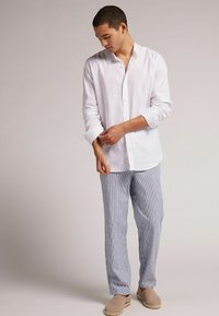 Camisa de lino blanca con botones, corte relajado y mangas largas. Pantalones rayados ligeros en azul y blanco combinados con alpargatas de color marrón claro.