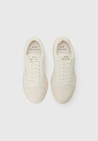Witte canvas sneakers met een gladde textuur, ronde neus en vetersluiting. Heeft subtiele merknaam op de zijkant en een lichtbeige zool.