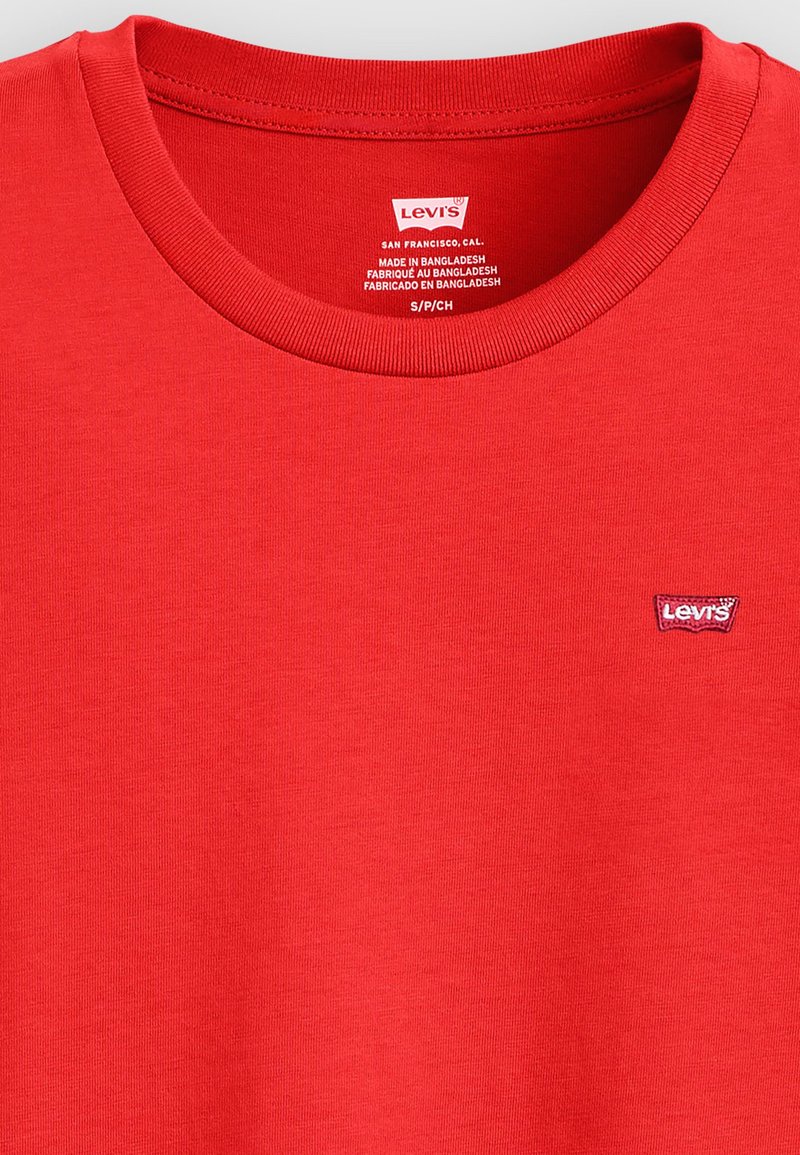 Camiseta de algodón roja con cuello redondo acanalado, que presenta un pequeño parche con el logo de Levi's en el lado izquierdo del pecho. Textura suave, diseño simple.