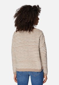 Beżowy i biały sweter w paski o luźnym kroju, z żebrowanymi mankietami i dołem, z teksturowanej dzianiny, noszony na niebieskich dżinsach.