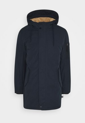 Parka d'hiver bleu marine foncé avec capuche doublée en polaire marron clair, fermeture éclair avant avec pressions, deux poches latérales et une poche zippée sur la manche.