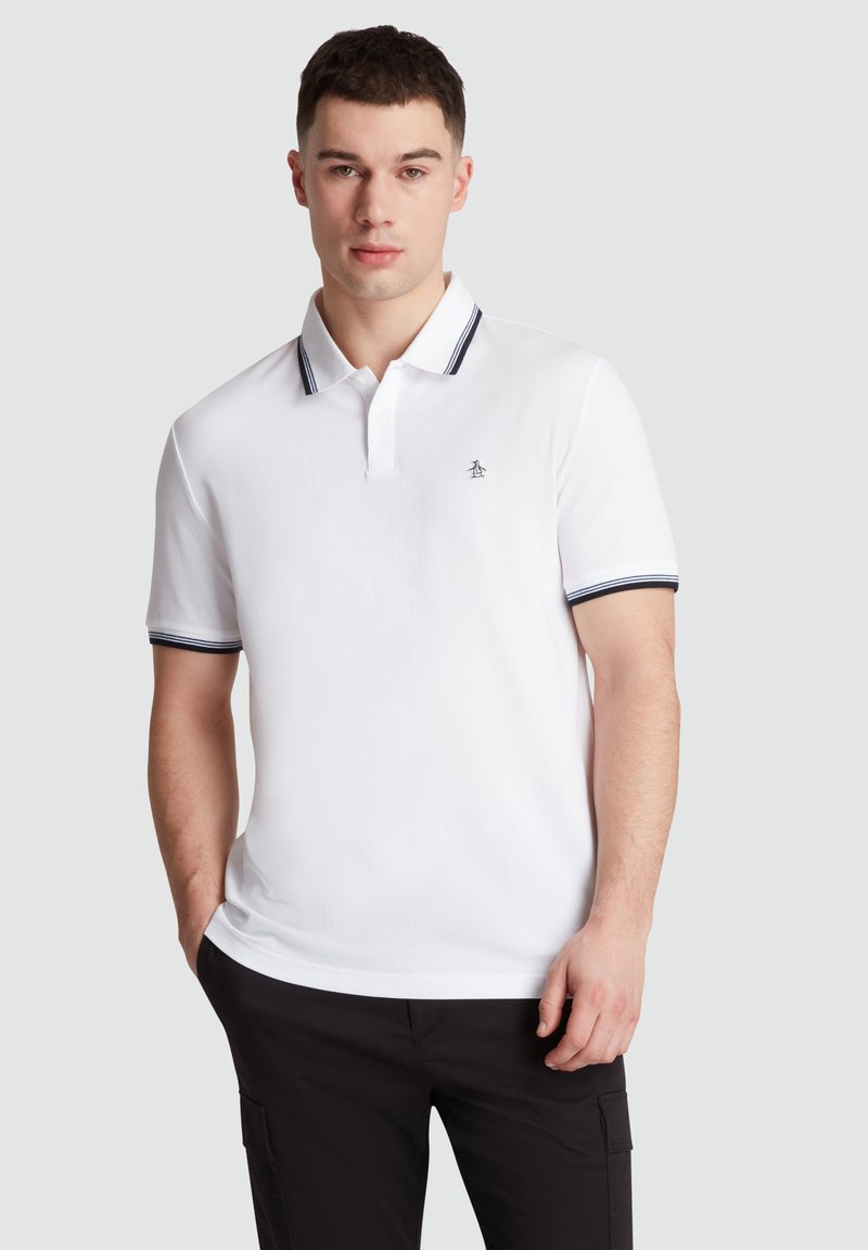 Witte polo met korte mouwen, voorzien van een marineblauwe gestreepte kraag en boorden, en een klein pinguïnlogo op de borst. Gladde textuur.