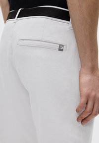 Pantalones de pana blanca con un acabado texturizado, que presentan un bolsillo trasero, cintura negra y un pequeño logo gris en el bolsillo.