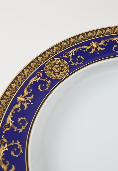 Apaļš porcelāna šķīvis ar zilu un zelta greznojumu, kas ietver sarežģītas ziedu rakstus un dekoratīvu apļveida akcentu malā.