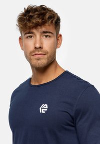 Camiseta de algodón de cuello redondo en azul marino, con un pequeño logo blanco en el área del pecho izquierdo y una textura suave y lisa.