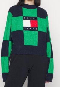 Grün- und marineblau karierter Pullover mit gerippter Textur. Verfügt über ein zentrales Logo-Patch in Weiß, Rot und Blau sowie ein kurzes Design.