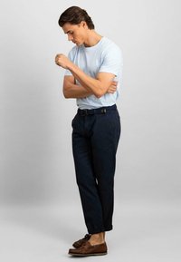 Tricou albastru deschis, pantaloni albaştri închis, pantofi de bărbați din piele maro. Pantalonii au o curea texturată cu o cataramă rectangulară.